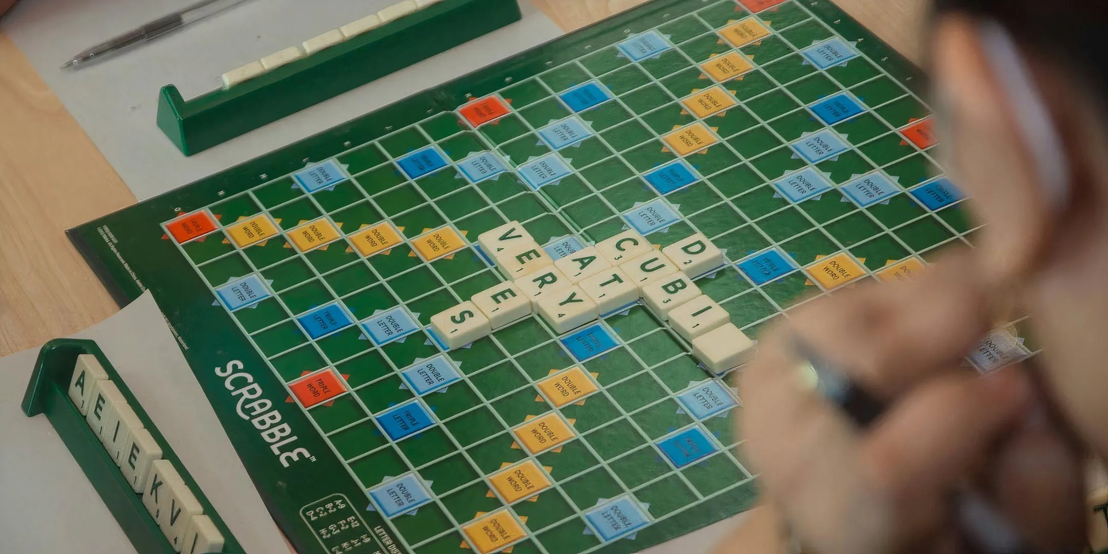 Bảng chơi Scrabble đang diễn ra với các quân cờ chữ, minh họa tình huống người chơi không tập trung lắng nghe hướng dẫn luật game.